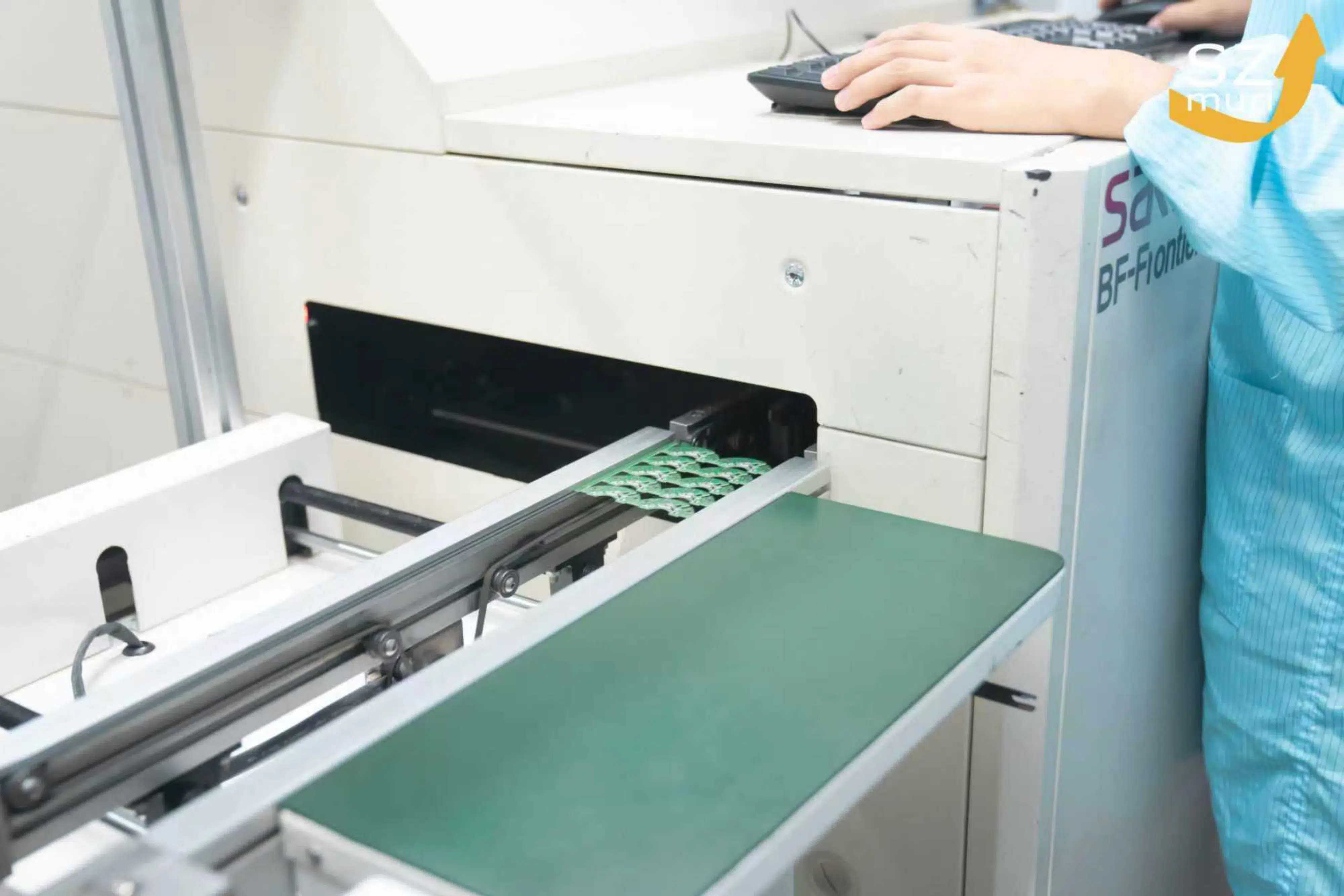 Eine Person in blauer Arbeitskleidung bedient eine Maschine mit grüner Ablagefläche