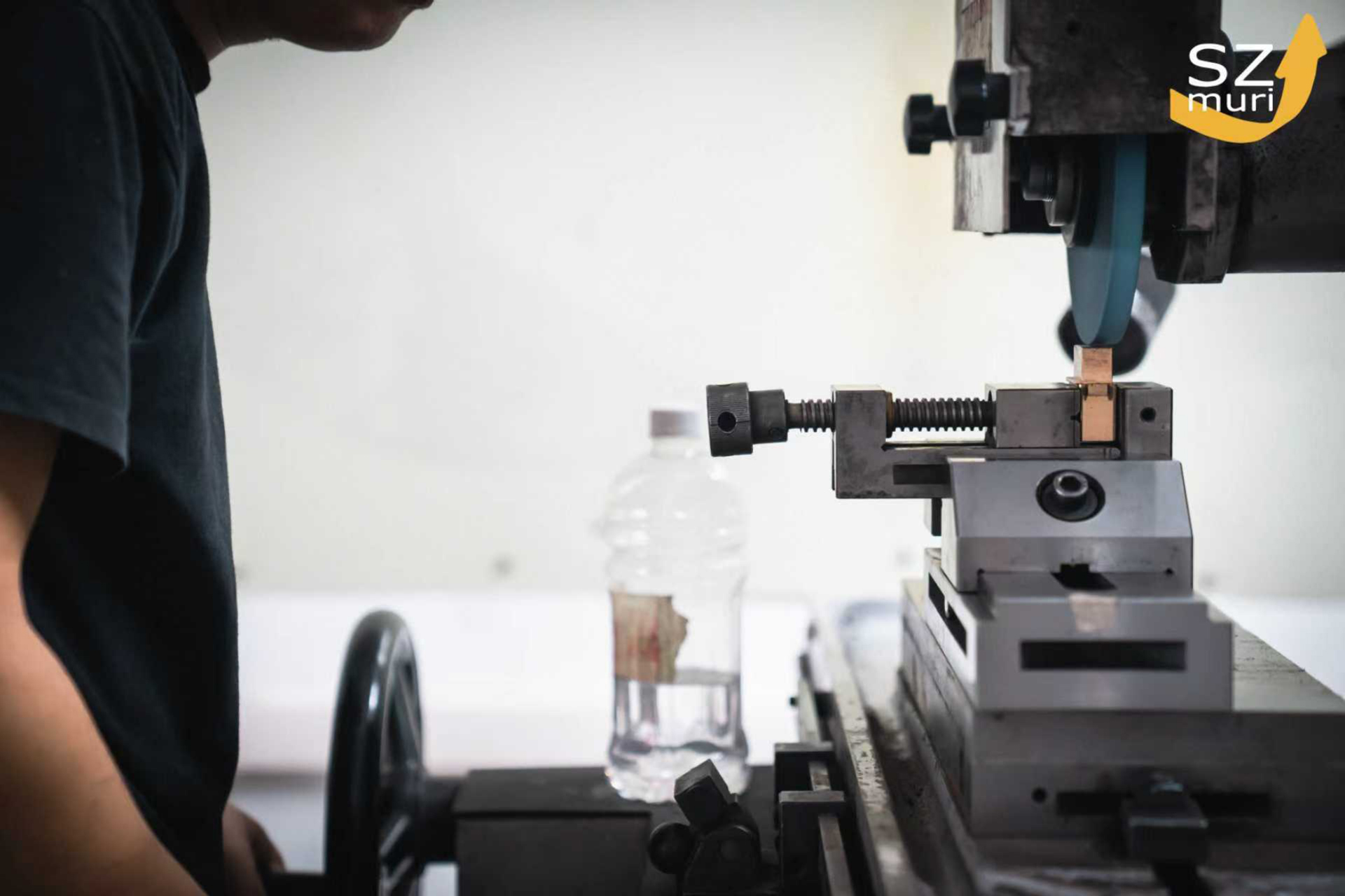 Eine Person steht neben einer Metallmaschine mit ernster Miene und einer Wasserflasche