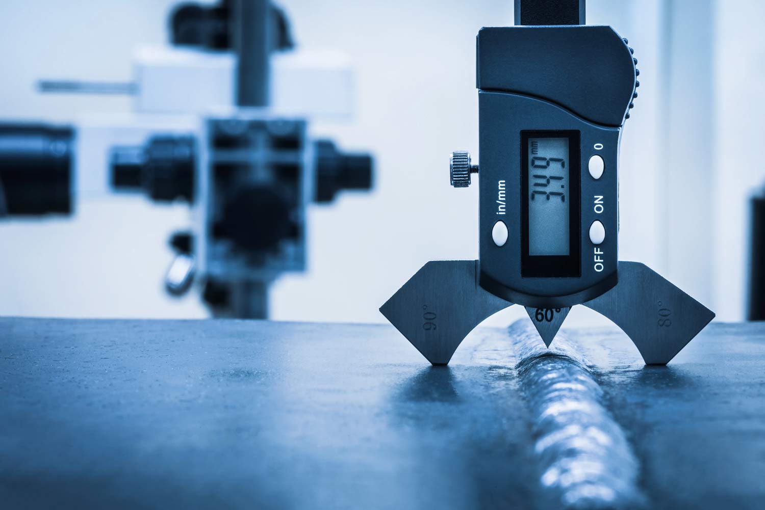 Ein digitales Messgerät misst eine silberne Schweißnaht auf einer blauen Metallplatte